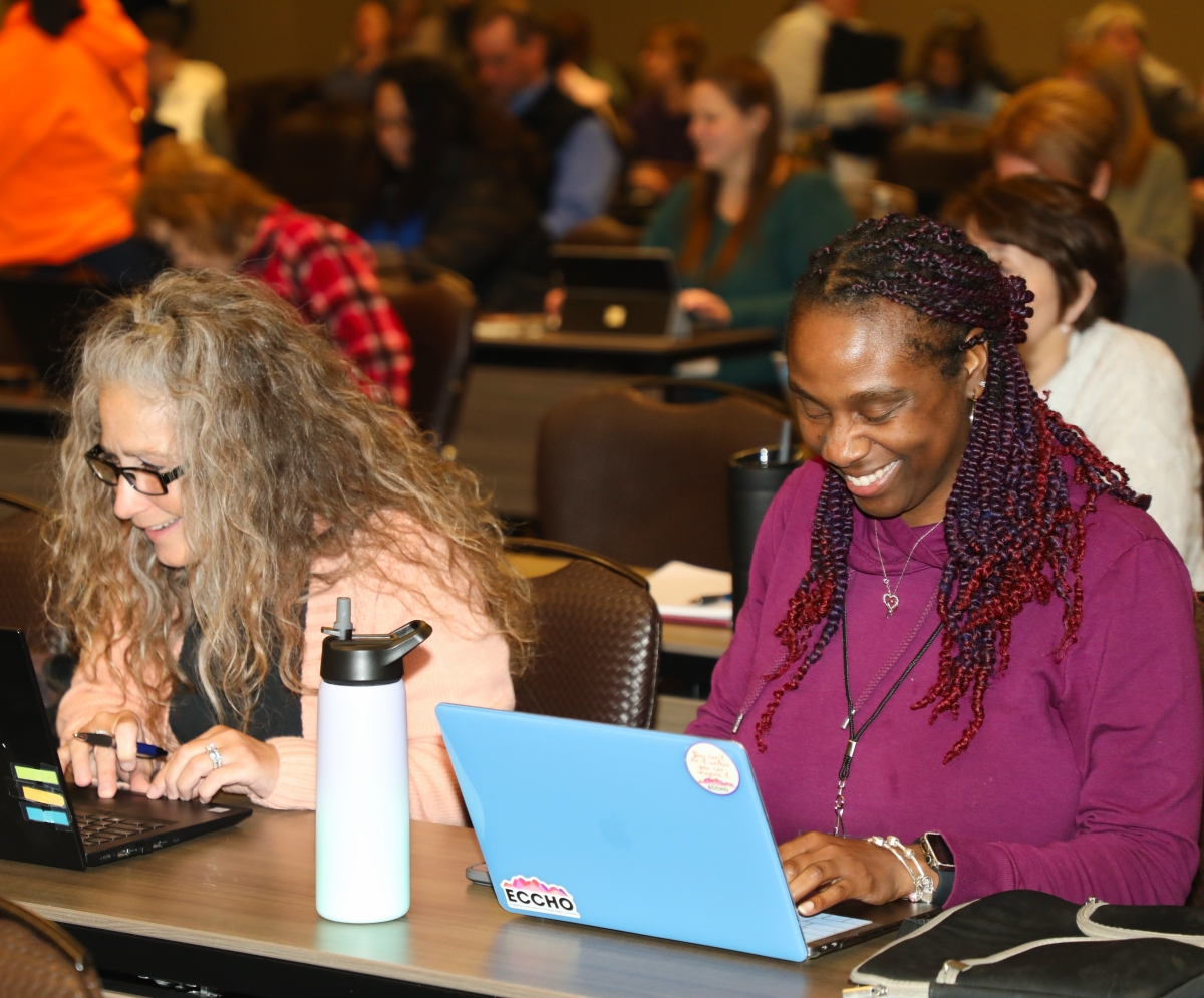 Two women smiling while they listen to infomration provided during the 8th annual WISEdata Conference
